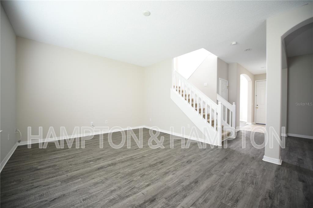 An empty living room features gray wood-look flooring, beige walls, and a white staircase — 2809 EAGLE CLAW COURT, KISSIMMEE, FL