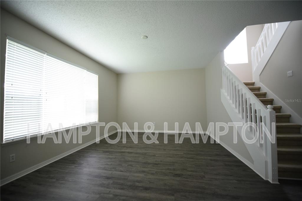An empty living room features wood-look flooring, a large window with blinds, and a staircase — 2809 EAGLE CLAW COURT, KISSIMMEE, FL