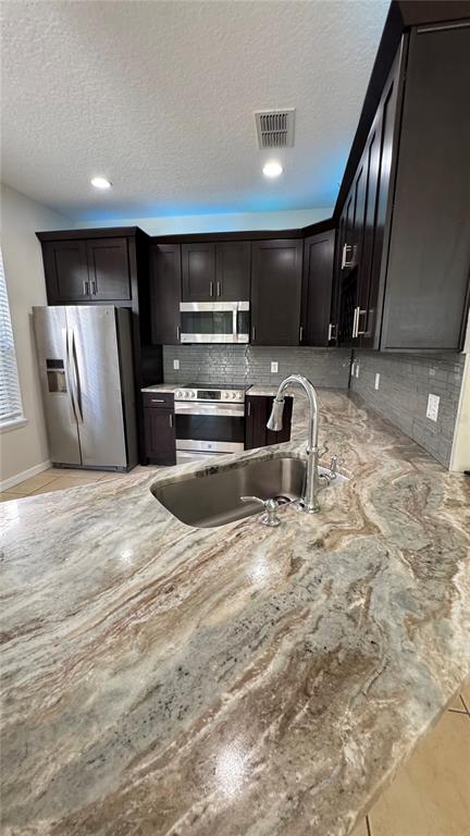 A kitchen features dark wood cabinets, stainless steel appliances, and a large patterned stone countertop — 6410 S GOLDENROD ROAD, ORLANDO, FL