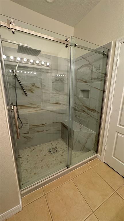 A walk-in shower features marble-look tile walls, a built-in bench, and a sliding glass door — 6410 S GOLDENROD ROAD, ORLANDO, FL
