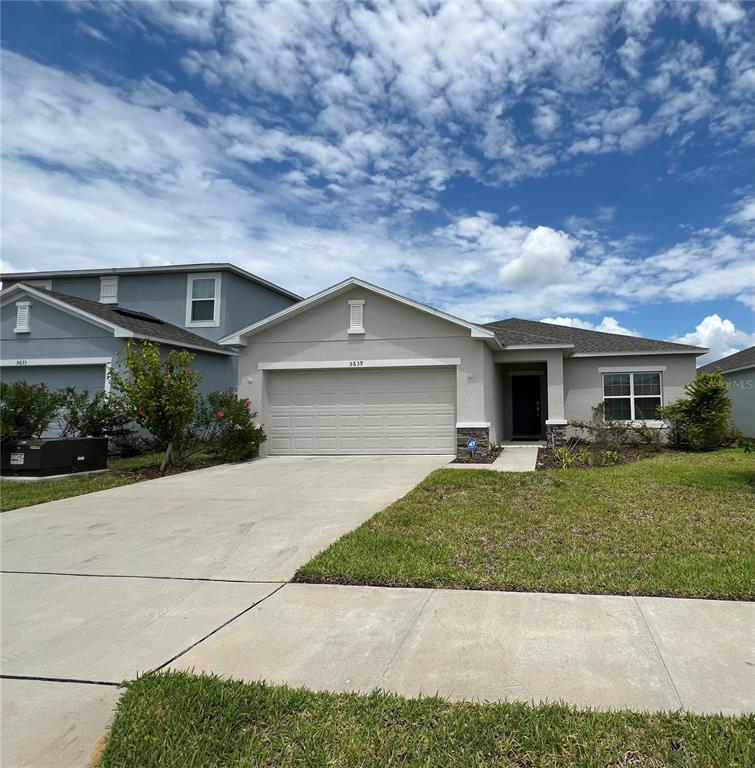 A single-story suburban house with a beige exterior, a two-car garage, and a front lawn — 5639 COSTA BLANCA WAY, DAVENPORT, FL