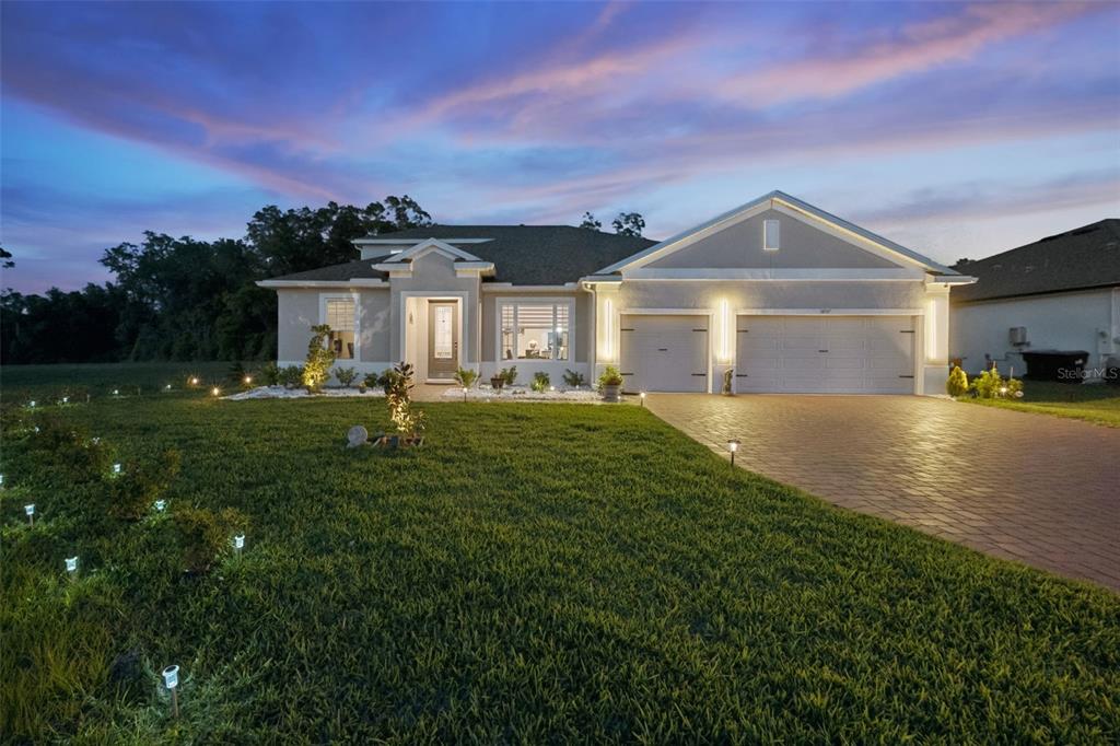 A single-story house with a paved driveway, two-car garage, and landscape lighting at dusk — 5897 SIERRA CROWN STREET, MOUNT DORA, FL