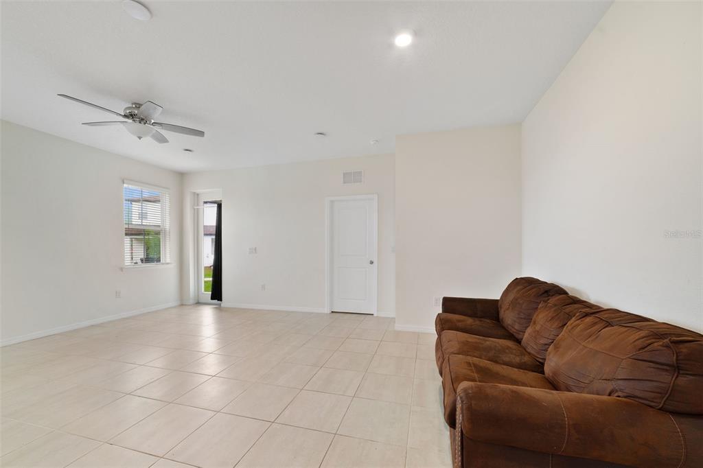 A living room with light tile flooring, a brown sofa, and a ceiling fan — 4371 CREEK COVE LANE, KISSIMMEE, FL