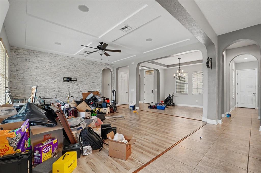 A living room with a stone accent wall, tray ceiling, and cluttered floor space — 31957 MARDELLE PLACE, WESLEY CHAPEL, FL