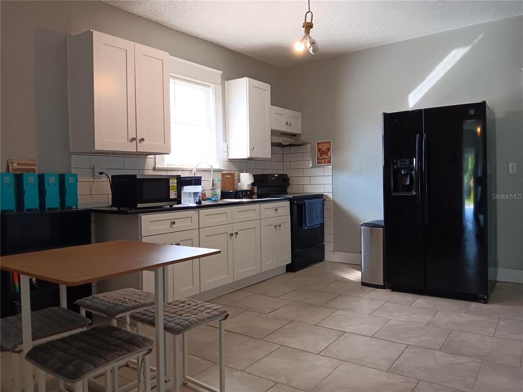 A kitchen features white cabinets, black appliances, a subway tile backsplash, and light tile flooring — 3508 E 28TH AVENUE, TAMPA, FL