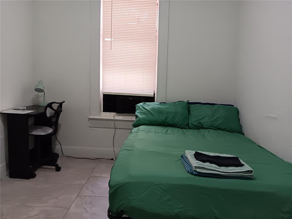 A bedroom features a bed with green bedding, a desk, and a window with blinds — 3508 E 28TH AVENUE, TAMPA, FL