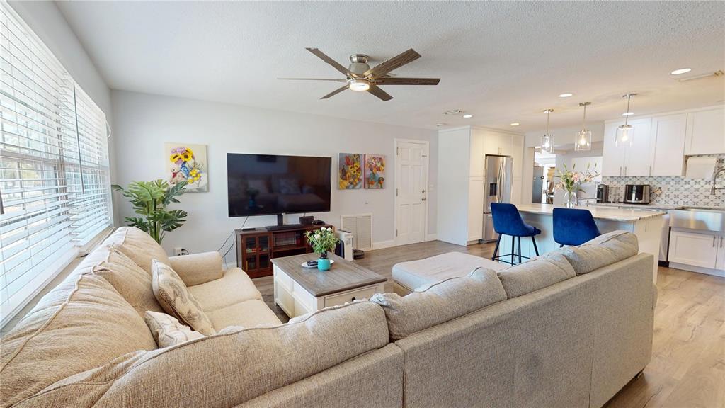 An open-concept living room features a sectional sofa, a television, and an adjacent kitchen — 2020 YALE AVENUE, DUNEDIN, FL