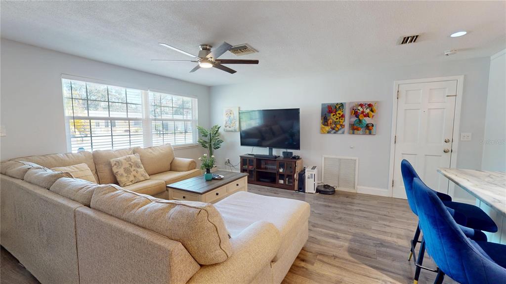 A living room features a beige sectional sofa, a television on a stand, and wood flooring — 2020 YALE AVENUE, DUNEDIN, FL