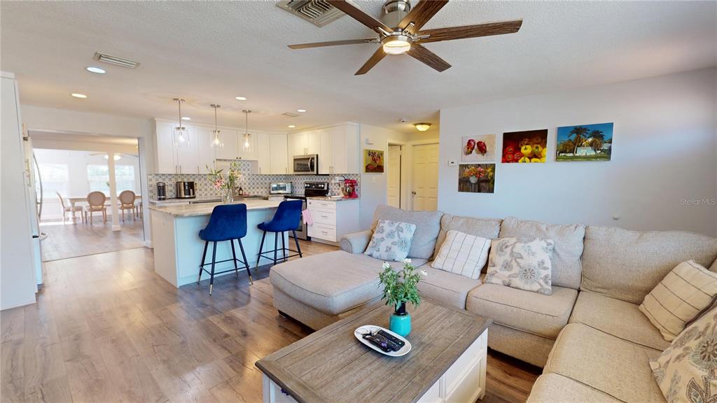 An open-concept living room features a sectional sofa, a coffee table, and a kitchen island — 2020 YALE AVENUE, DUNEDIN, FL