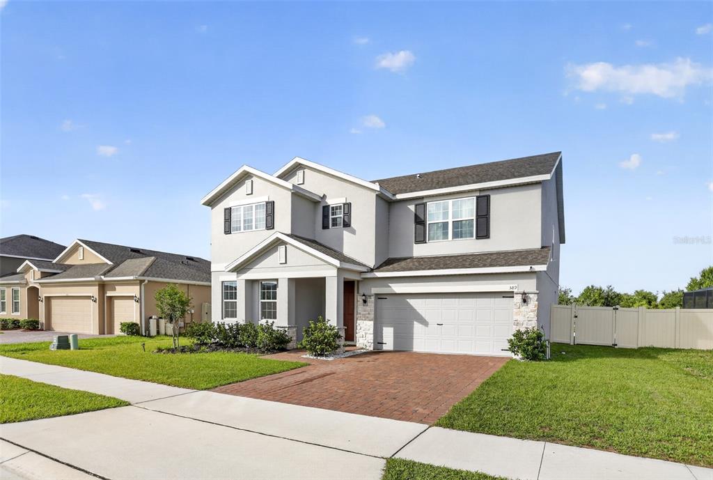 A two-story suburban house with a gray stucco exterior, stone accents, and a paved driveway — 589 JUPITER BEACH ROAD, GROVELAND, FL