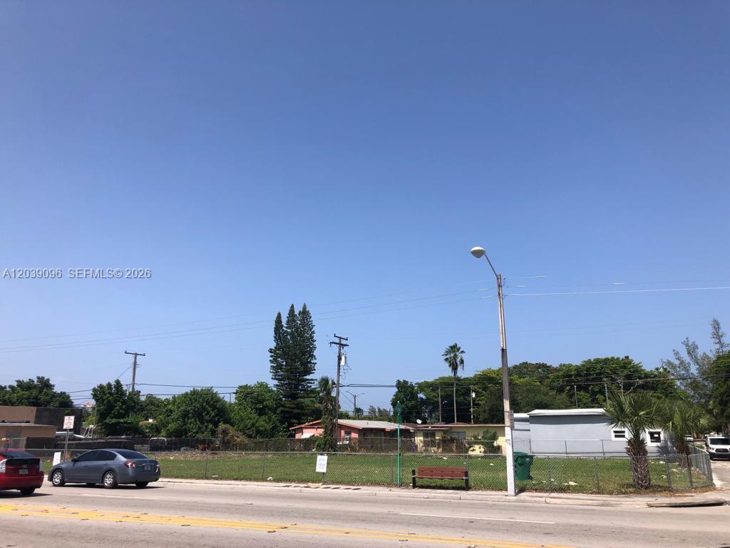 A vacant, fenced-in grassy lot sits along a paved road under a clear blue sky — 4923 NW 17th Ave, Miami FL 33142, MIAMI, FL