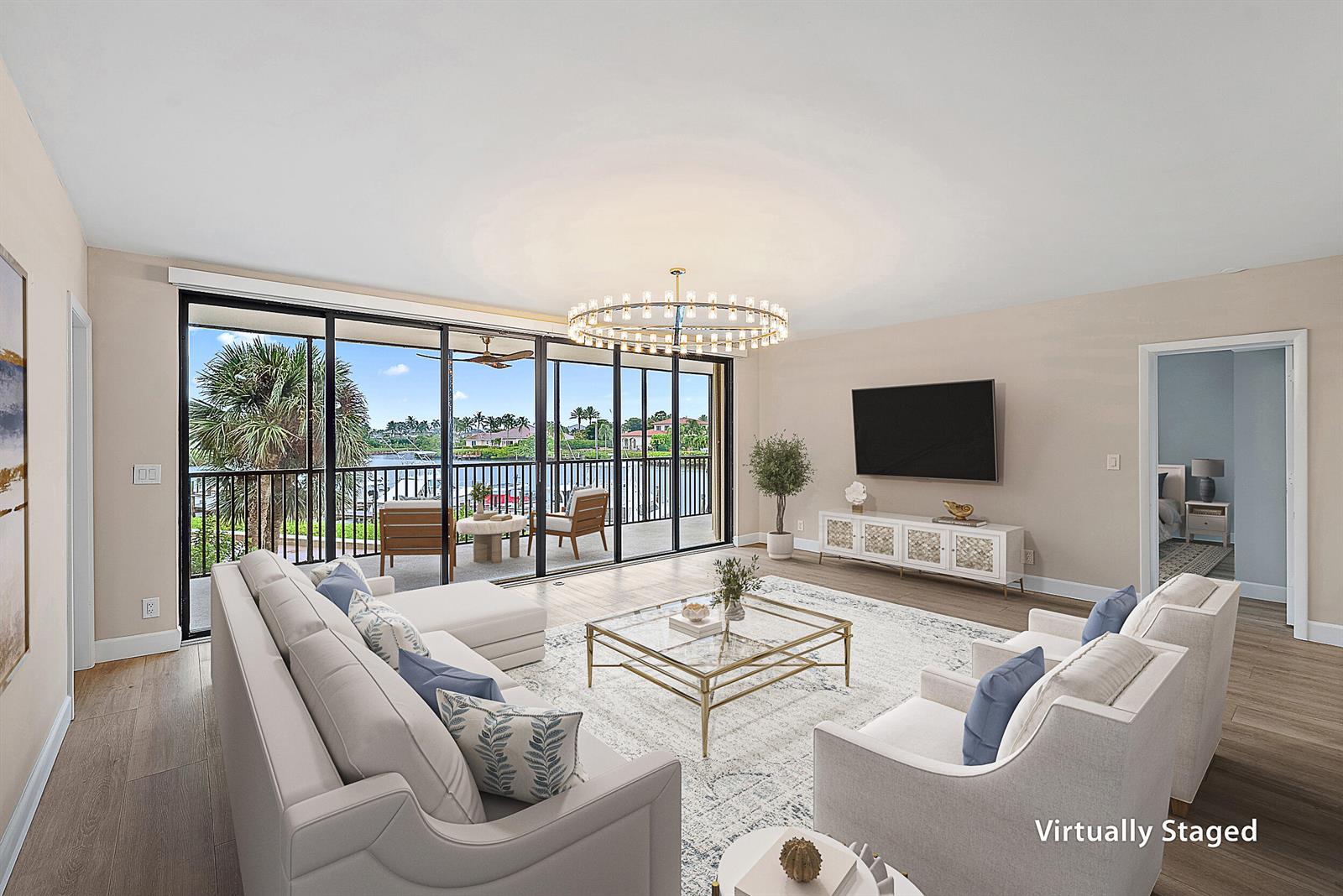 A virtually staged living room features a sectional, armchairs, and sliding doors overlooking a waterway — 16910 Bay Street # E204, Jupiter FL 33477, JUPITER, FL