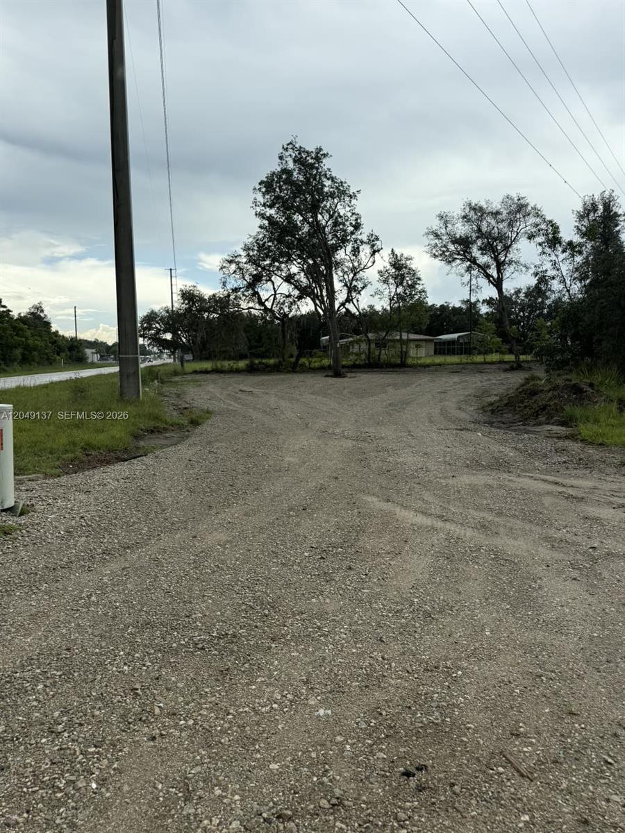 A gravel driveway leads to a vacant lot with several trees under a cloudy sky — 4732 Kenilworth Blvd, Sebring FL 33872, SEBRING, FL
