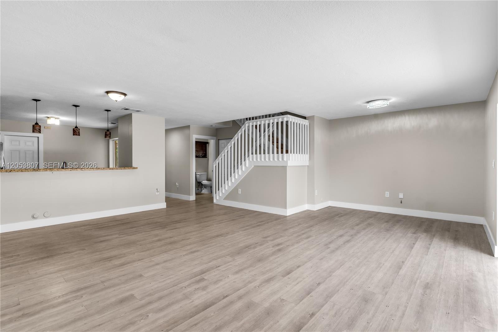 An open living area features light wood-look flooring, a staircase with white railings, and a kitchen — 7463 SW 164th Ave, Miami FL 33193, MIAMI, FL
