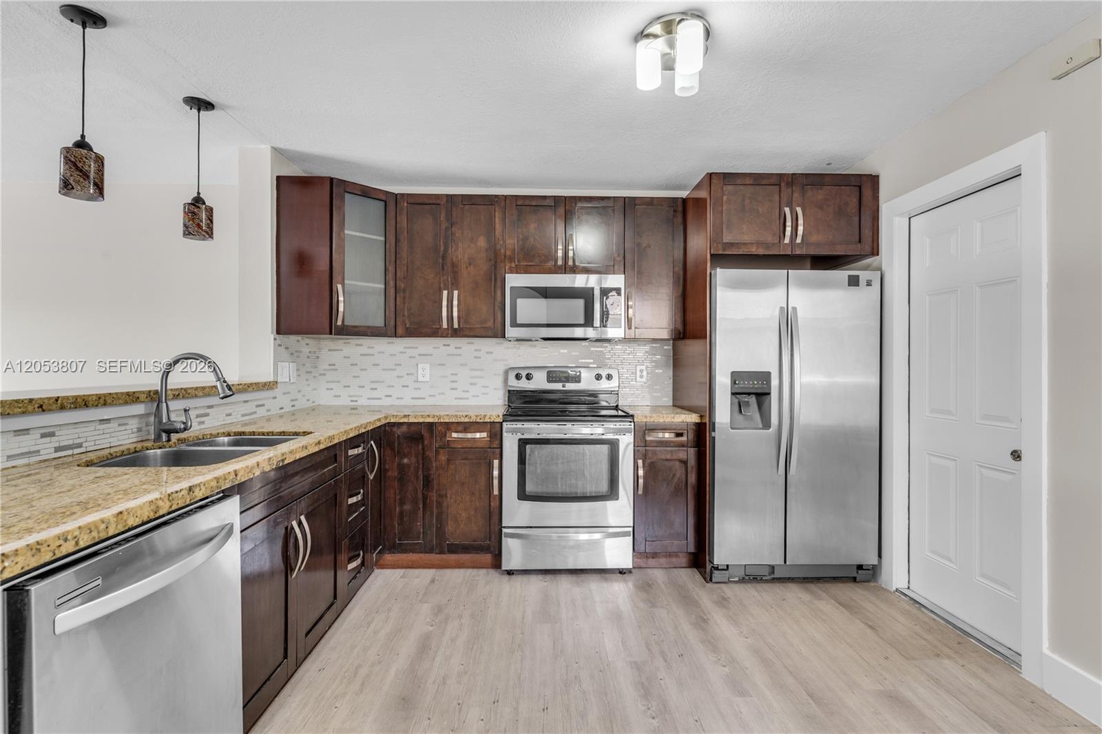 A kitchen features dark wood cabinets, stainless steel appliances, granite countertops, and light wood flooring — 7463 SW 164th Ave, Miami FL 33193, MIAMI, FL