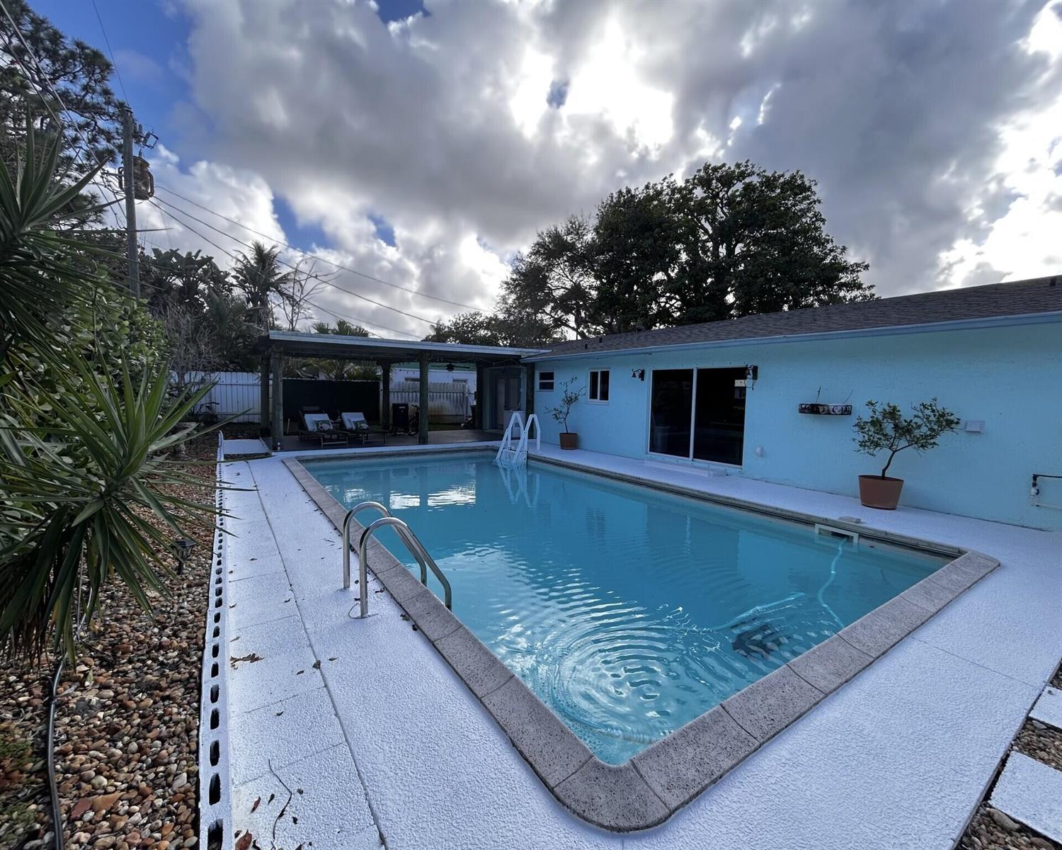 A backyard features a rectangular swimming pool with a white deck and a covered patio — 1301 SE Sandpiper Lane, Stuart FL 34996, STUART, FL