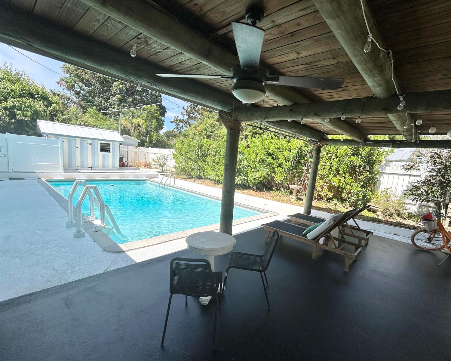 A covered patio overlooks a swimming pool with lounge chairs and a small bistro set — 1301 SE Sandpiper Lane, Stuart FL 34996, STUART, FL