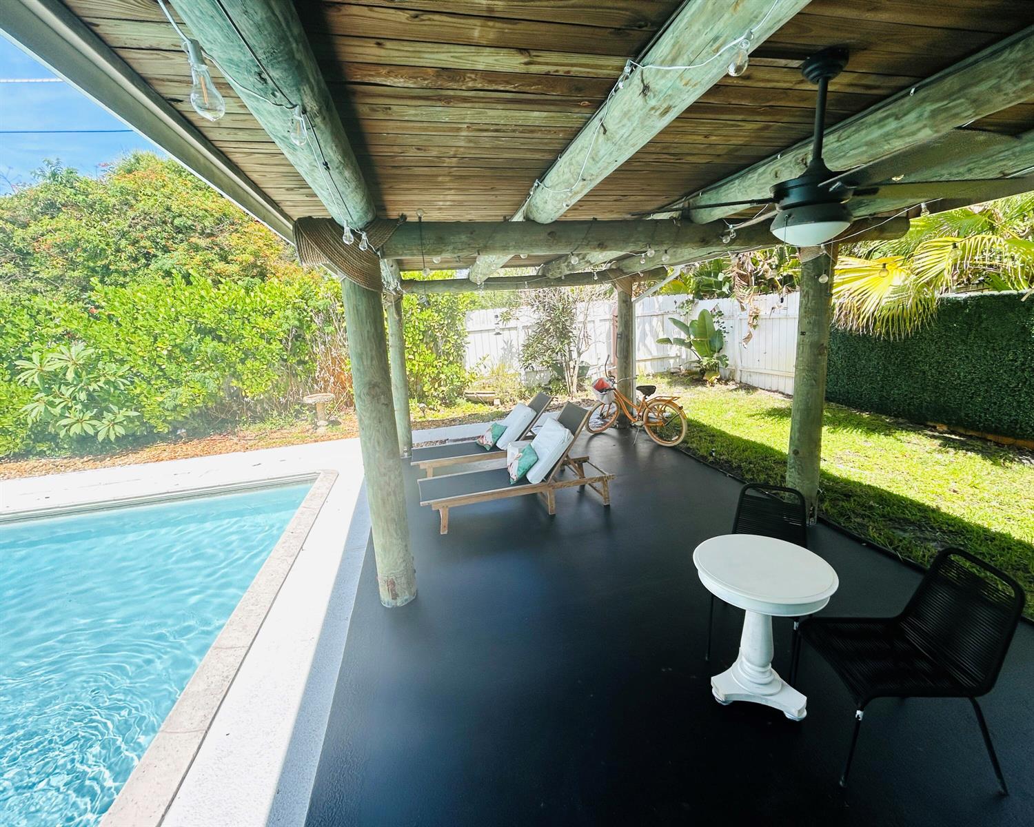 A covered patio with a black floor, lounge chairs, a small table, and a pool — 1301 SE Sandpiper Lane, Stuart FL 34996, STUART, FL