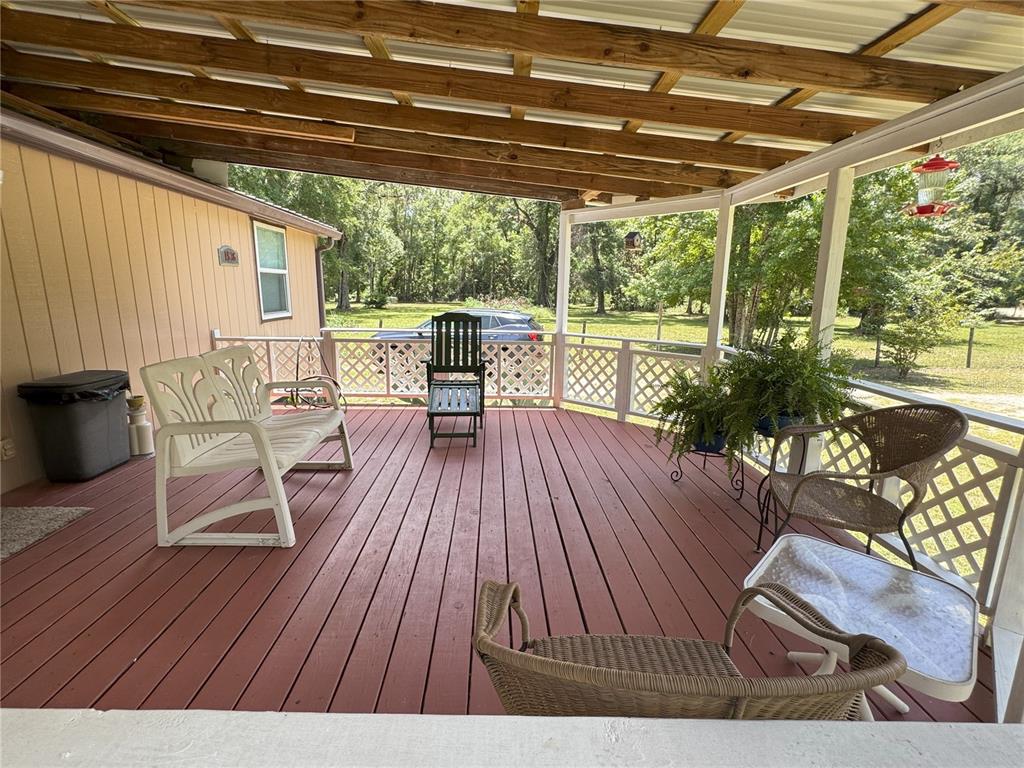 A covered wooden deck features outdoor furniture, a white lattice railing, and a view of trees — 1536 NE 592ND STREET, OLD TOWN, FL