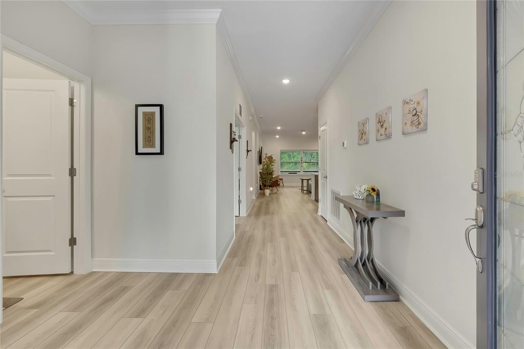 A bright entryway leads down a long hallway with light wood-look flooring toward a living area — 32 CARNATION COURT, HOMOSASSA, FL