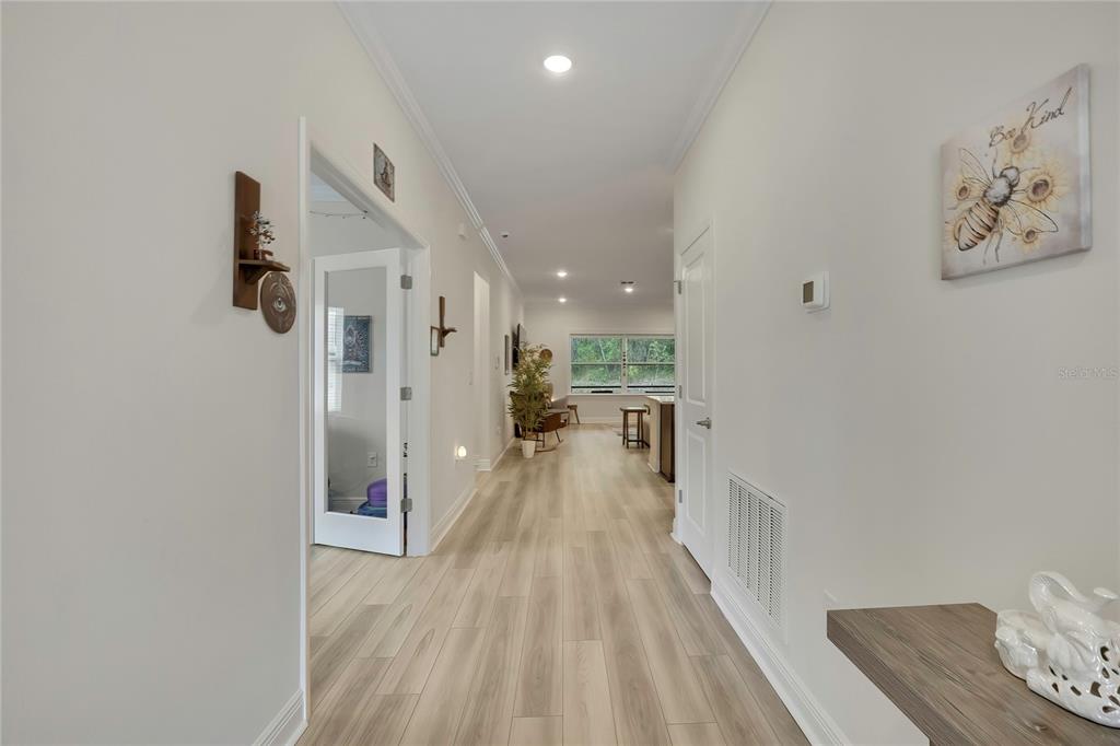 A hallway with light wood-look flooring leads toward an open-concept living area with a window — 32 CARNATION COURT, HOMOSASSA, FL