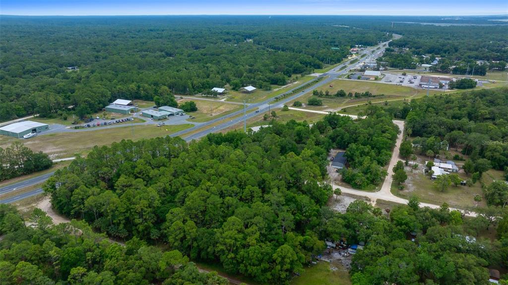 An aerial view shows a wooded lot adjacent to a highway and commercial buildings — RACHEL AVE & HWY 19 N, INGLIS, FL