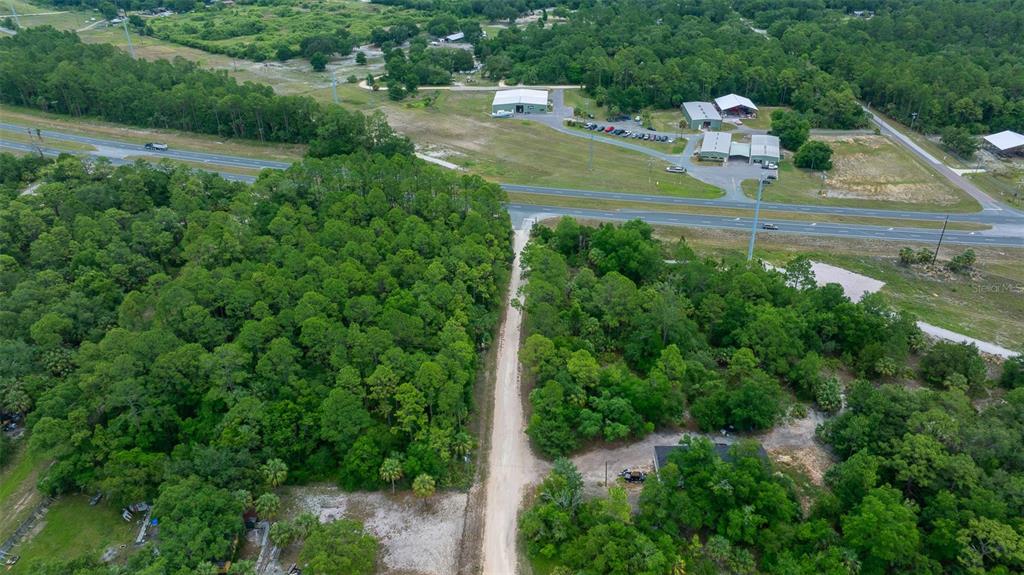 An aerial view shows a dirt road leading to a wooded lot near a highway — RACHEL AVE & HWY 19 N, INGLIS, FL