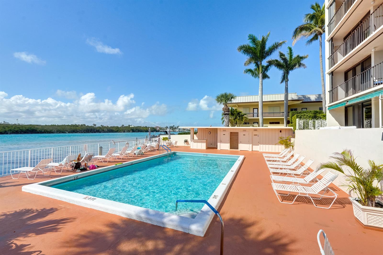 A swimming pool sits on a patio next to a building and a waterway — 225 Beach Road # 503, Tequesta FL 33469, TEQUESTA, FL