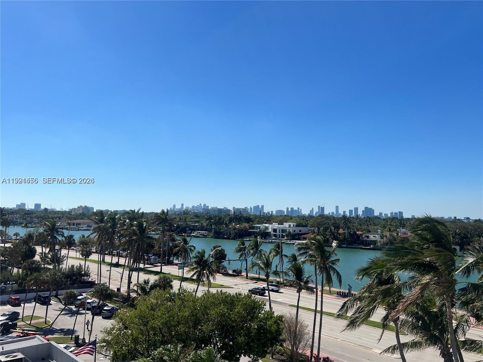 An elevated view shows a coastal road, palm trees, a waterway, and a distant city skyline — 5313 Collins Ave # 704, Miami Beach FL 33140, MIAMI BEACH, FL