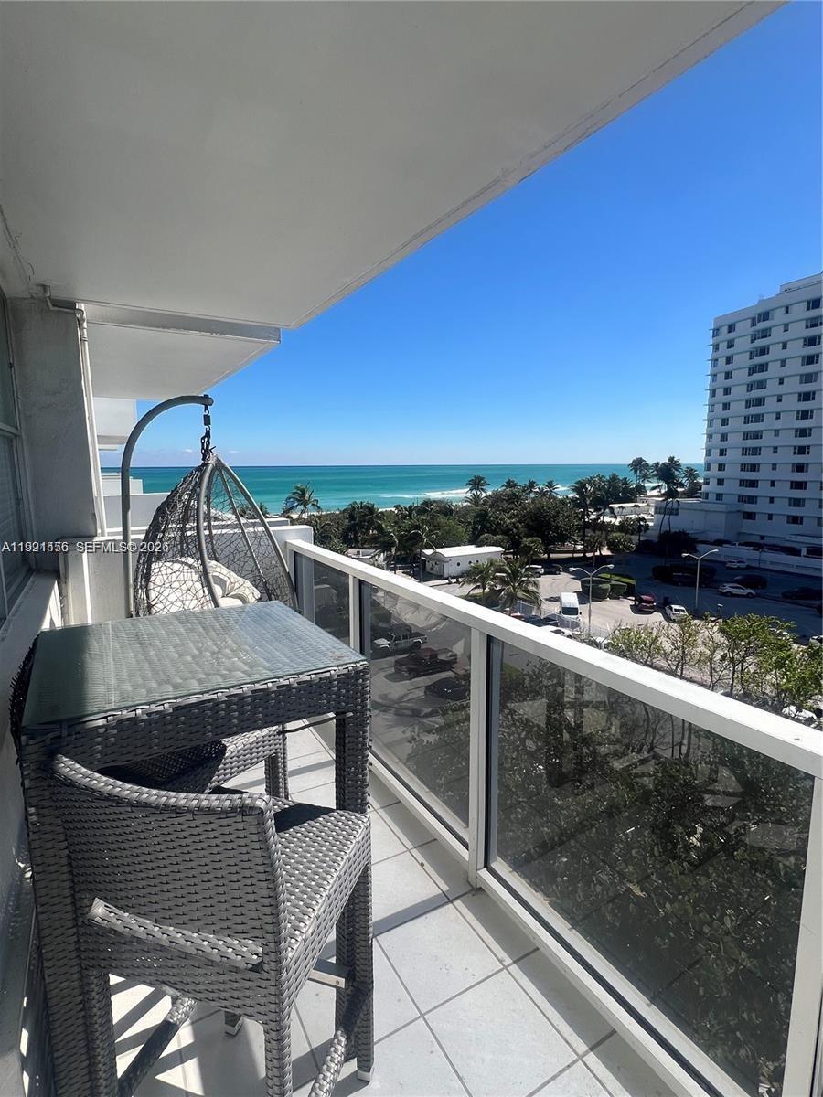 A balcony features a glass-topped table, two chairs, a hanging chair, and an ocean view — 5313 Collins Ave # 704, Miami Beach FL 33140, MIAMI BEACH, FL