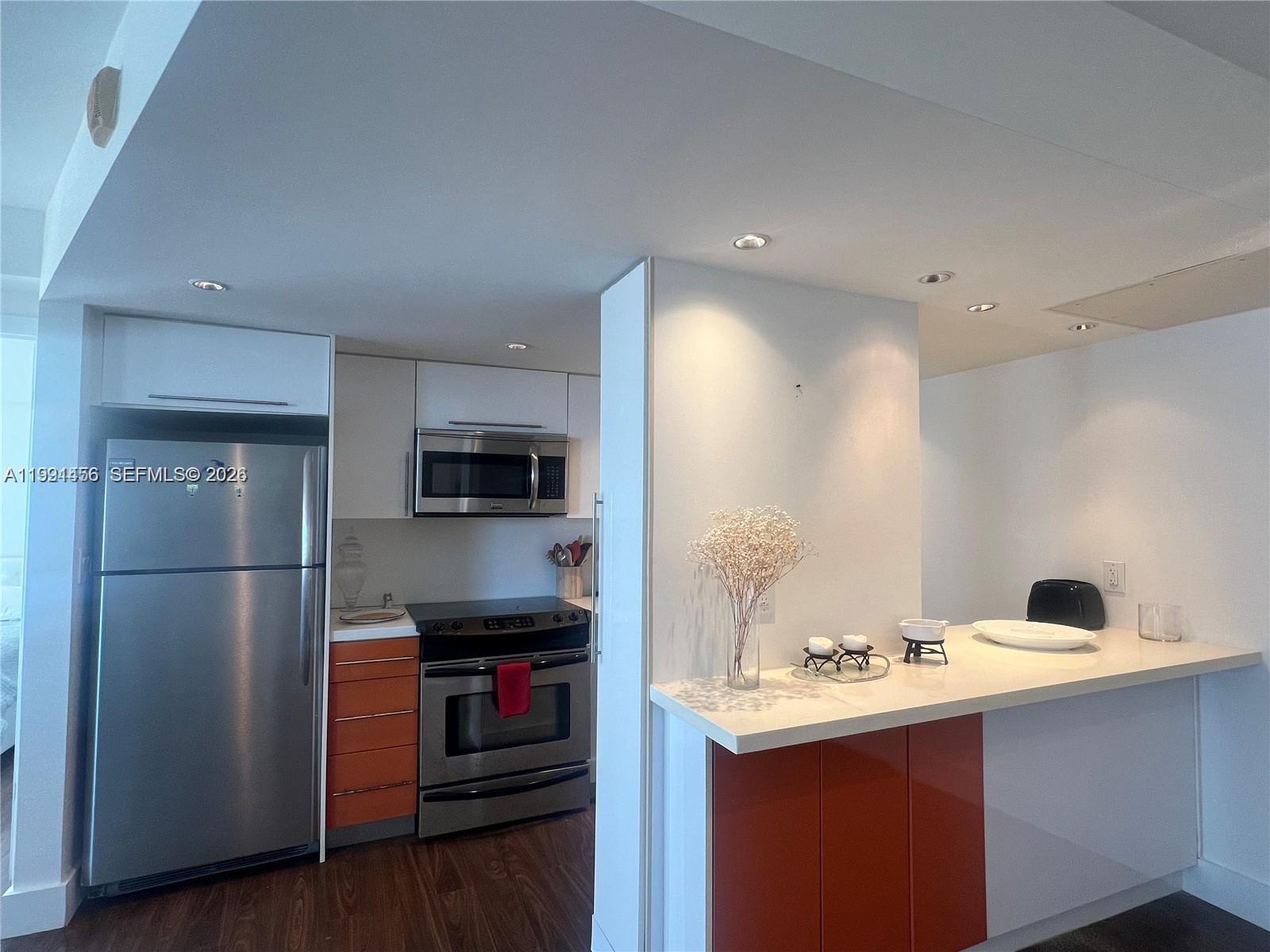 A kitchen features stainless steel appliances, orange and white cabinetry, and a white breakfast bar — 5313 Collins Ave # 704, Miami Beach FL 33140, MIAMI BEACH, FL