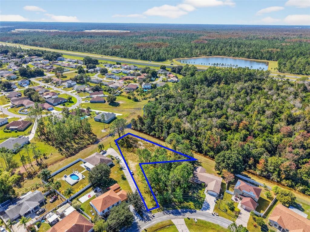 An aerial view shows a vacant, wooded residential lot outlined in blue within a neighborhood — 955 CAMBRIDGE COURT, KISSIMMEE, FL