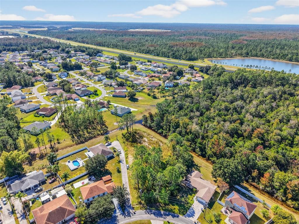 An aerial view shows a suburban neighborhood with houses, swimming pools, and surrounding wooded areas — 955 CAMBRIDGE COURT, KISSIMMEE, FL