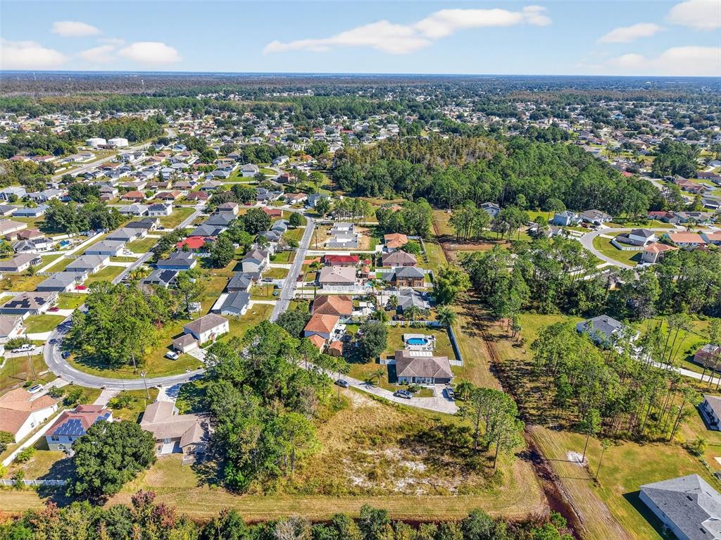 An aerial view shows a suburban neighborhood with houses, trees, and a large vacant lot — 955 CAMBRIDGE COURT, KISSIMMEE, FL