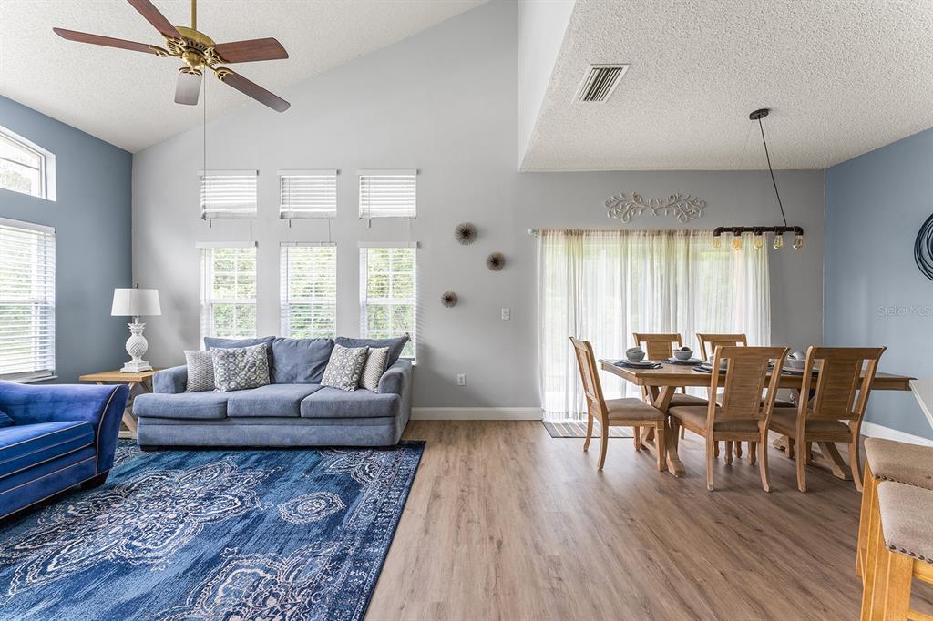 A living and dining area with vaulted ceilings, blue walls, wood flooring, and a ceiling fan — 2739 SUN KEY PLACE, KISSIMMEE, FL