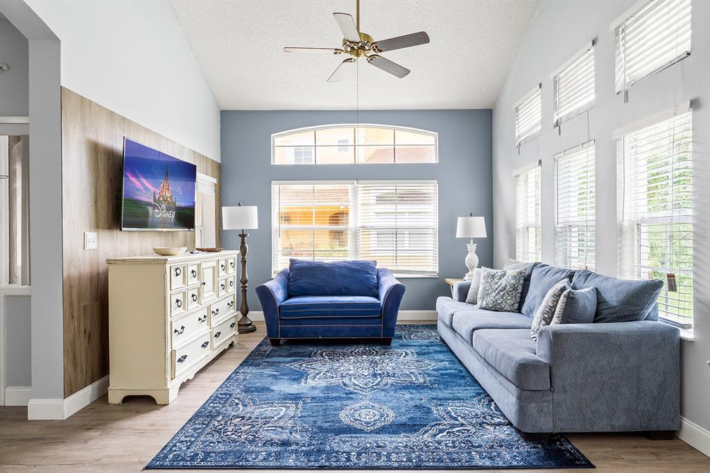 A living room features a blue sofa, a matching armchair, and a wood-paneled accent wall — 2739 SUN KEY PLACE, KISSIMMEE, FL