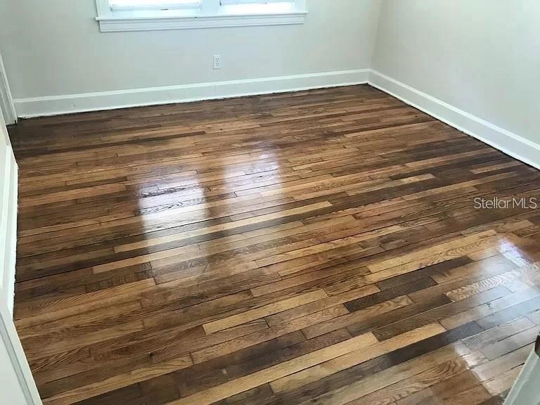 An empty room features polished hardwood flooring with varied wood tones and white baseboards — 545 15TH AVENUE S, ST PETERSBURG, FL