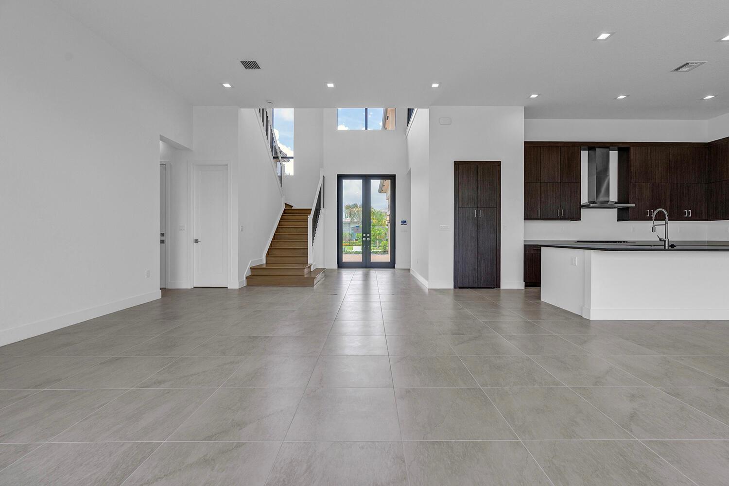 A modern open-concept living area features gray tile floors, a staircase, and a dark kitchen — 9523 Riverside Park Drive, Boca Raton FL 33434, BOCA RATON, FL