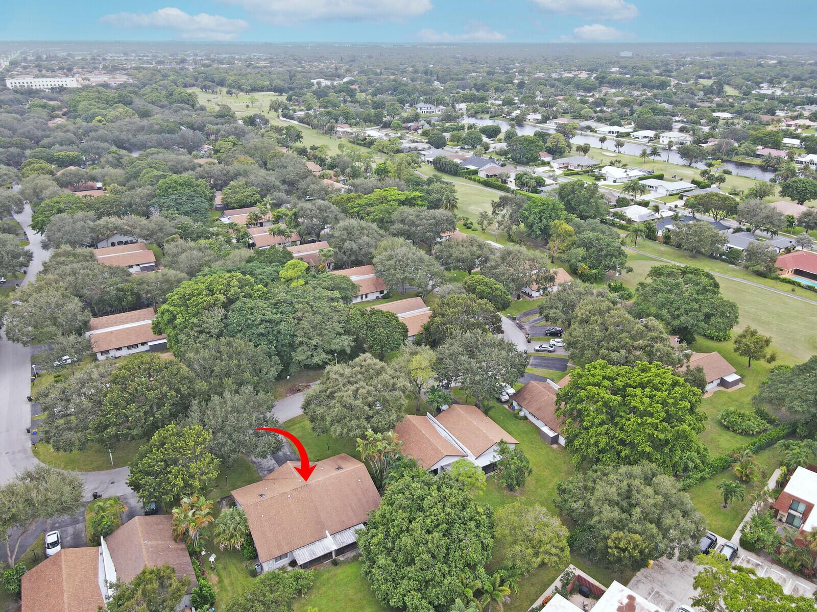 An aerial view shows a residential neighborhood with brown-roofed houses surrounded by many trees — 3680 ARELIA Drive S, Delray Beach FL 33445, DELRAY BEACH, FL