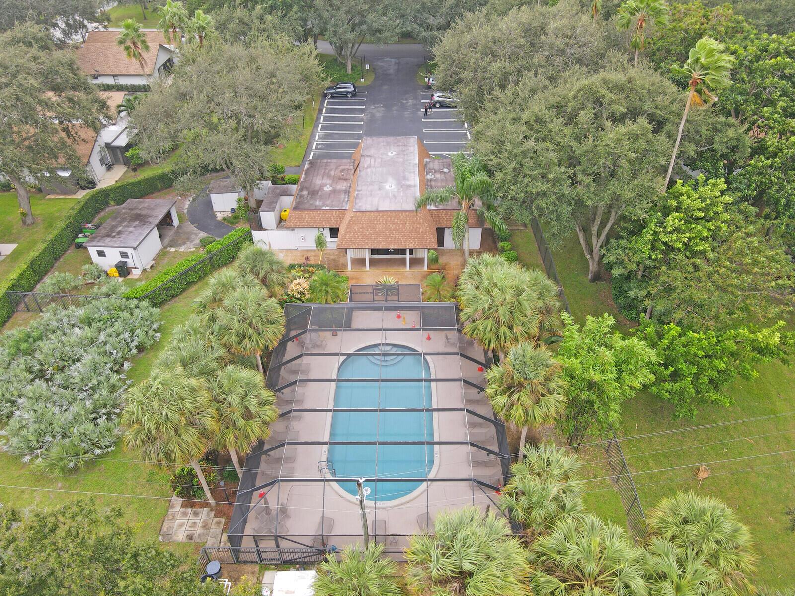 An aerial view shows a community clubhouse with a screened-in swimming pool and parking lot — 3680 ARELIA Drive S, Delray Beach FL 33445, DELRAY BEACH, FL