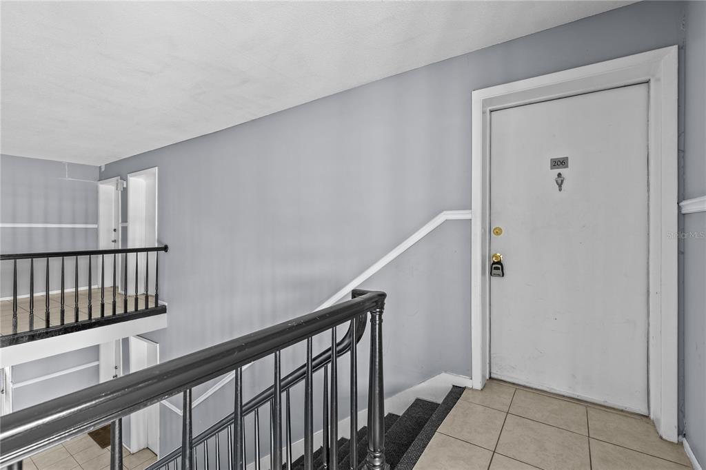 A white door labeled 206 sits at the top of a staircase with black railings — 416 BANYON TREE CIRCLE UNIT 206, MAITLAND, FL