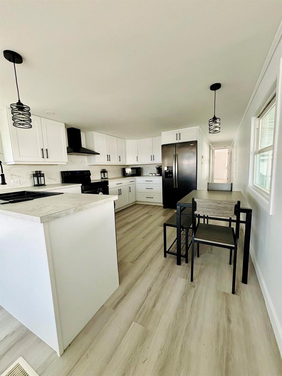 A modern kitchen features white cabinets, black appliances, a central island, and light wood flooring — 3003 Bimini Bay, Boynton Beach FL 33436, BOYNTON BEACH, FL
