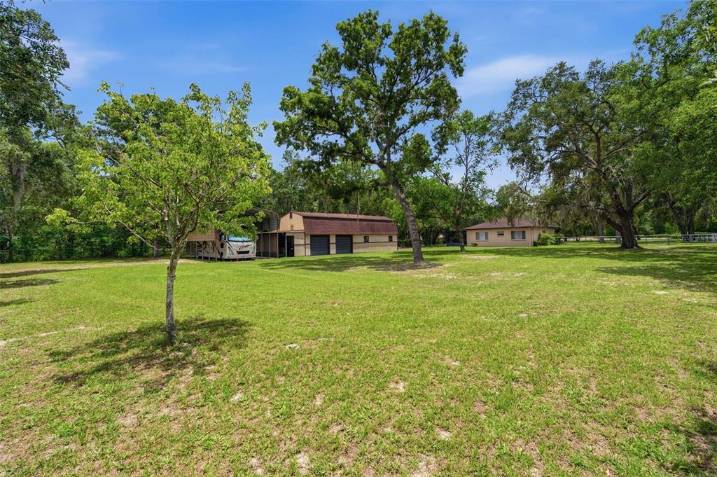 A large grassy yard features a detached garage with a carport and a separate house — 15041 CAMROSE AVENUE, SPRING HILL, FL