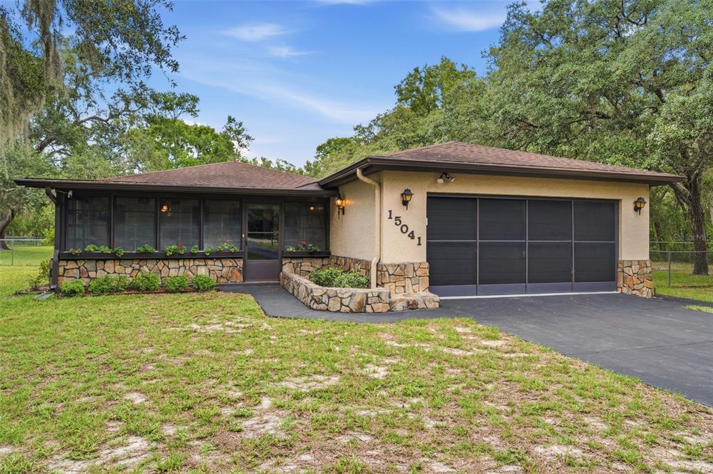 A single-story house with a stone facade, a screened-in porch, and a two-car garage — 15041 CAMROSE AVENUE, SPRING HILL, FL