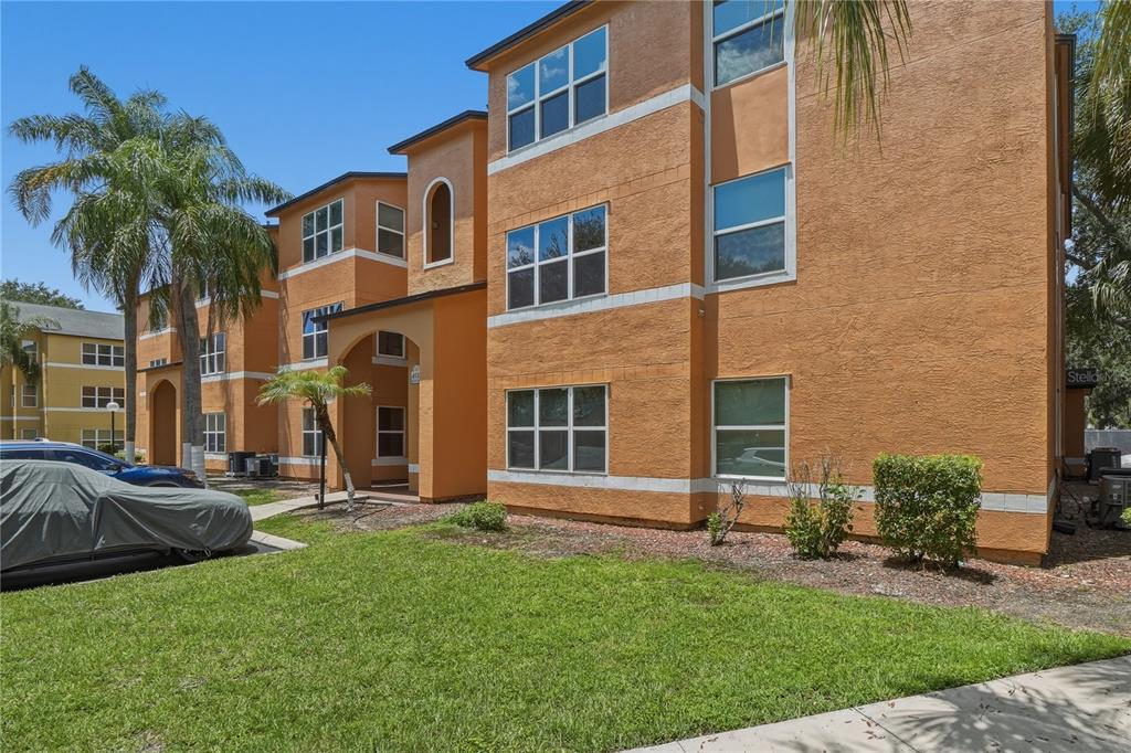 A three-story orange apartment building with a covered entrance and a lawn in front — 4532 COMMANDER DRIVE UNIT 2121, ORLANDO, FL
