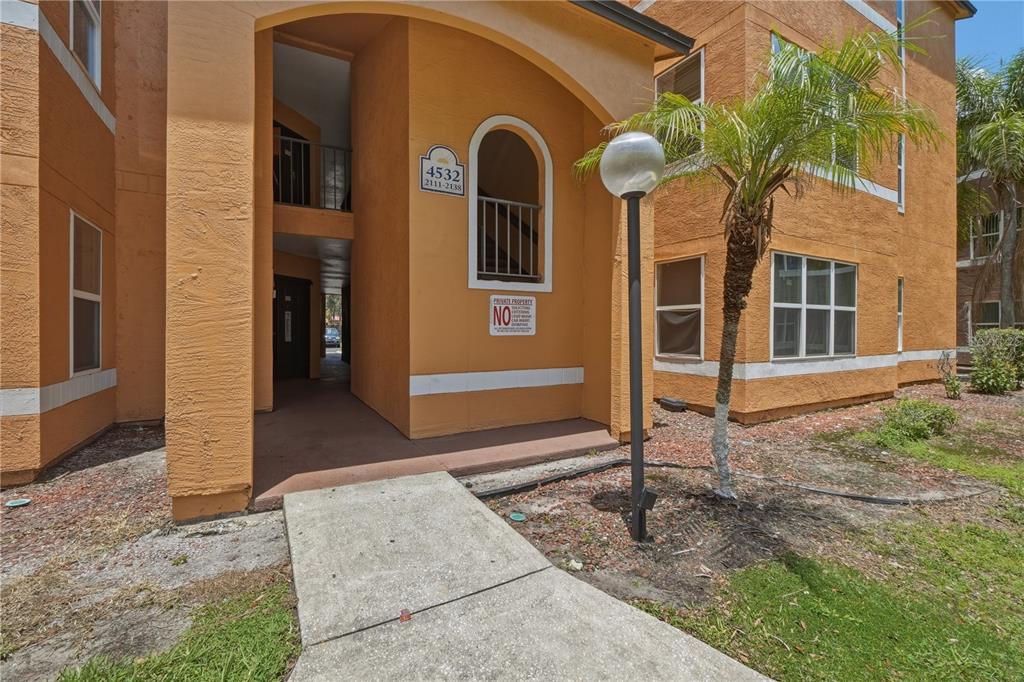 A concrete walkway leads to the entrance of an orange stucco apartment building — 4532 COMMANDER DRIVE UNIT 2121, ORLANDO, FL