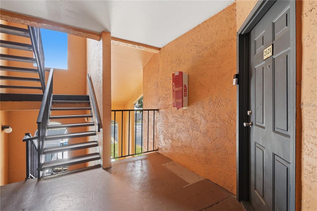 An outdoor apartment landing features a dark door, a fire extinguisher, and metal stairs — 4532 COMMANDER DRIVE UNIT 2121, ORLANDO, FL