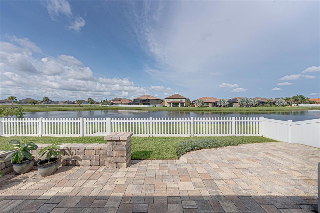 A paved patio overlooks a grassy lawn, a white picket fence, and a lake — 11947 SAND MYRTLE ROAD, RIVERVIEW, FL