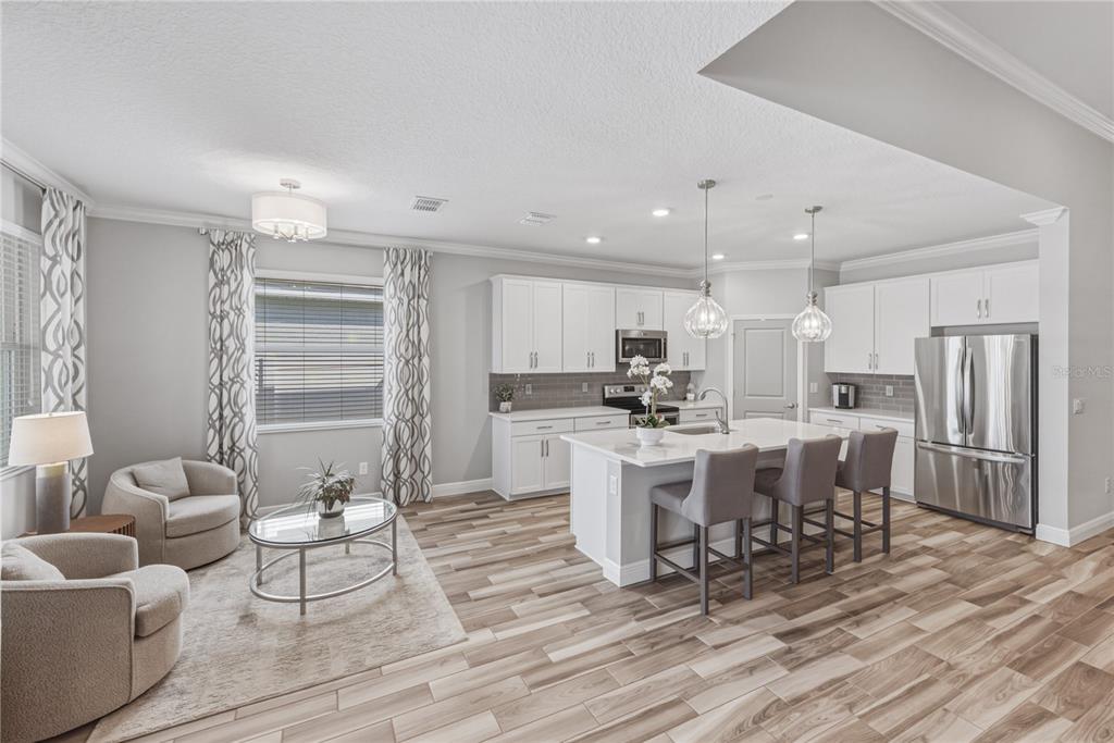 A bright open-concept kitchen and living area featuring white cabinetry, a center island, and wood-look flooring — 11947 SAND MYRTLE ROAD, RIVERVIEW, FL