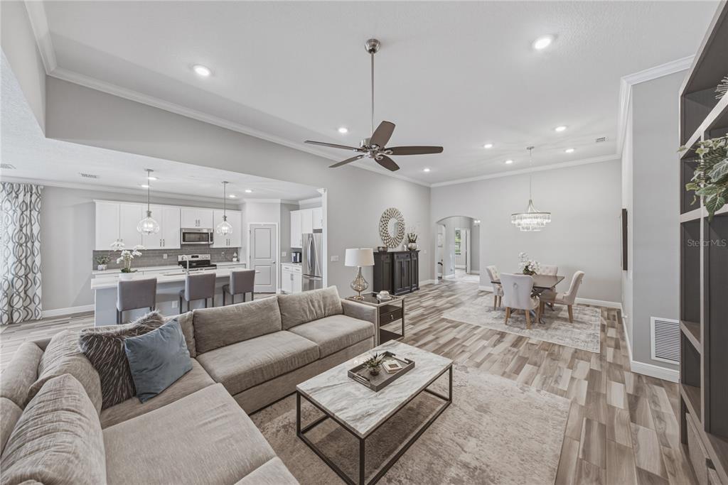 An open-concept living room, dining area, and kitchen with light wood flooring and neutral decor — 11947 SAND MYRTLE ROAD, RIVERVIEW, FL